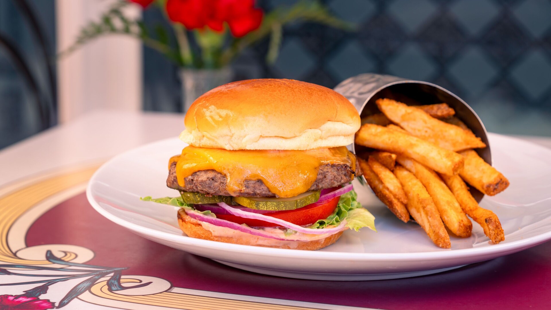Cheeseburger with cheddar, pickles, tomato, red onion, and lettuce on a brioche bun, served with a cup of fries at Carnation Café. | CREDIT: Disney