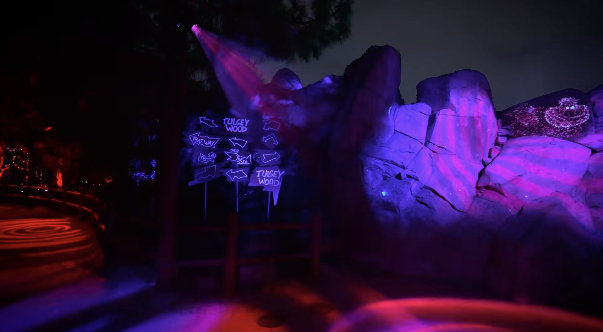 Glowing Tulgey Wood direction signs beside pink and purple lit rockwork inside Villains Grove. | CREDIT: Disney
