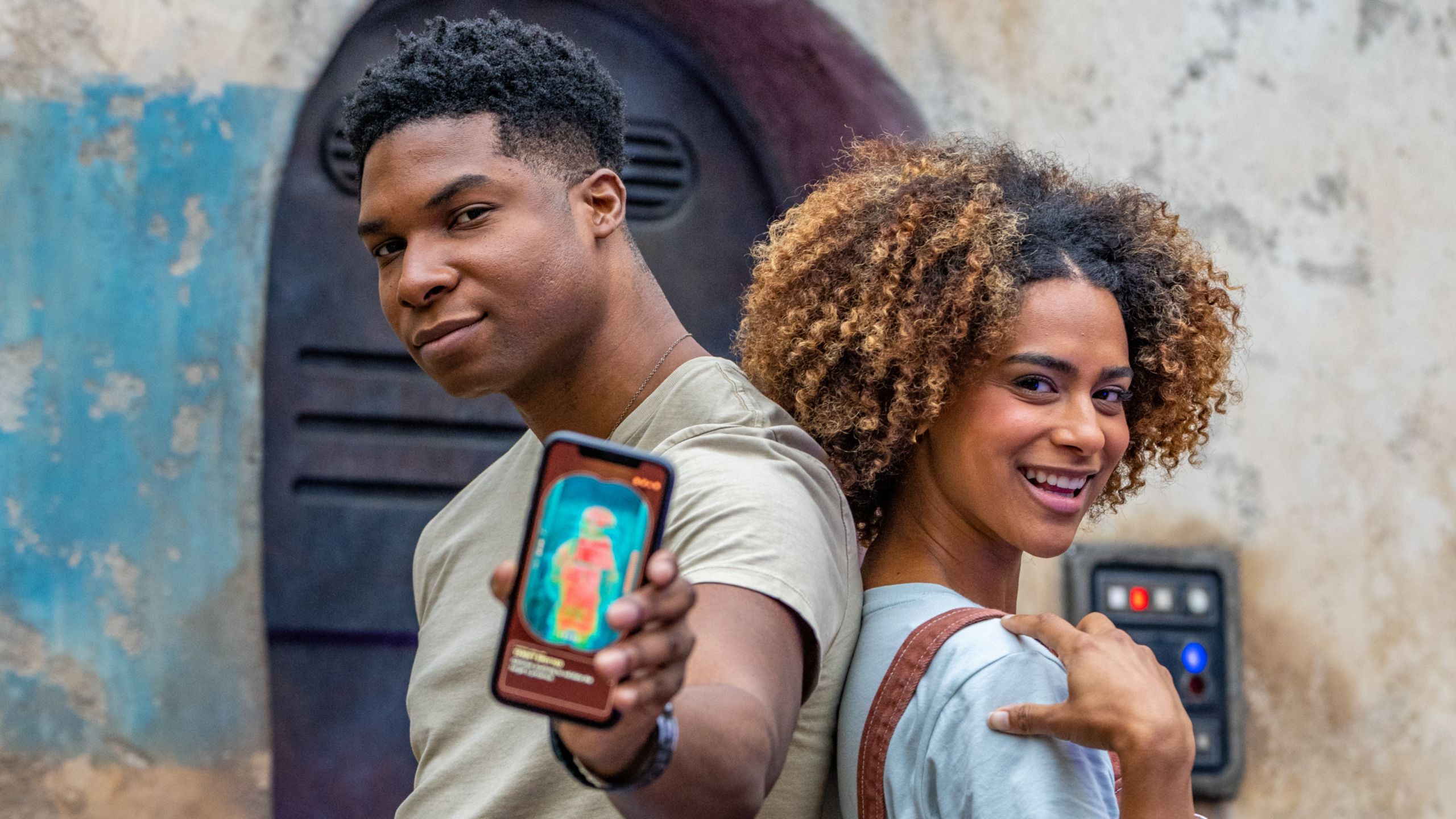 Two guests track a bounty target on a phone beside a Batuu Bounty Hunters screen in Star Wars: Galaxy's Edge. | CREDIT: Disney