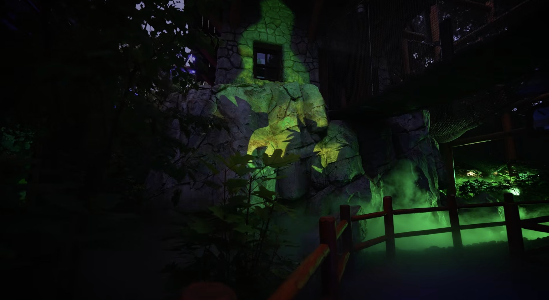 A large shadow projected onto rockwork in green and yellow light with fog at its base. | CREDIT: Disney