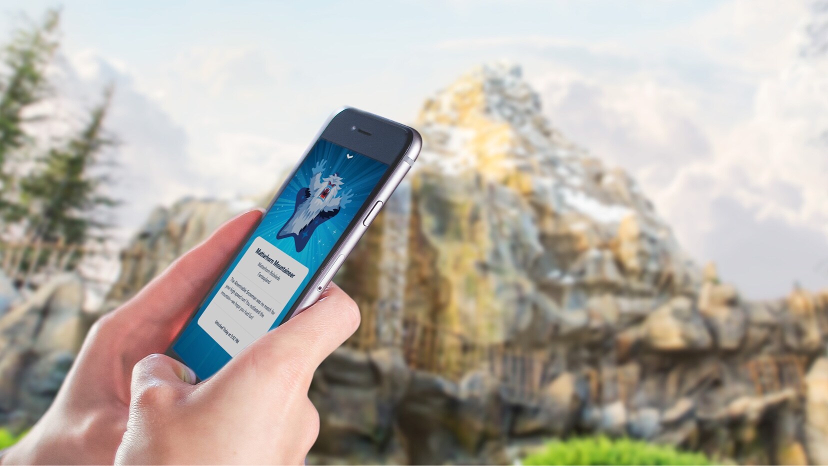 A guest holds up a phone showing a Play Disney Parks digital achievement in front of the Matterhorn at Disneyland. | CREDIT: Disney