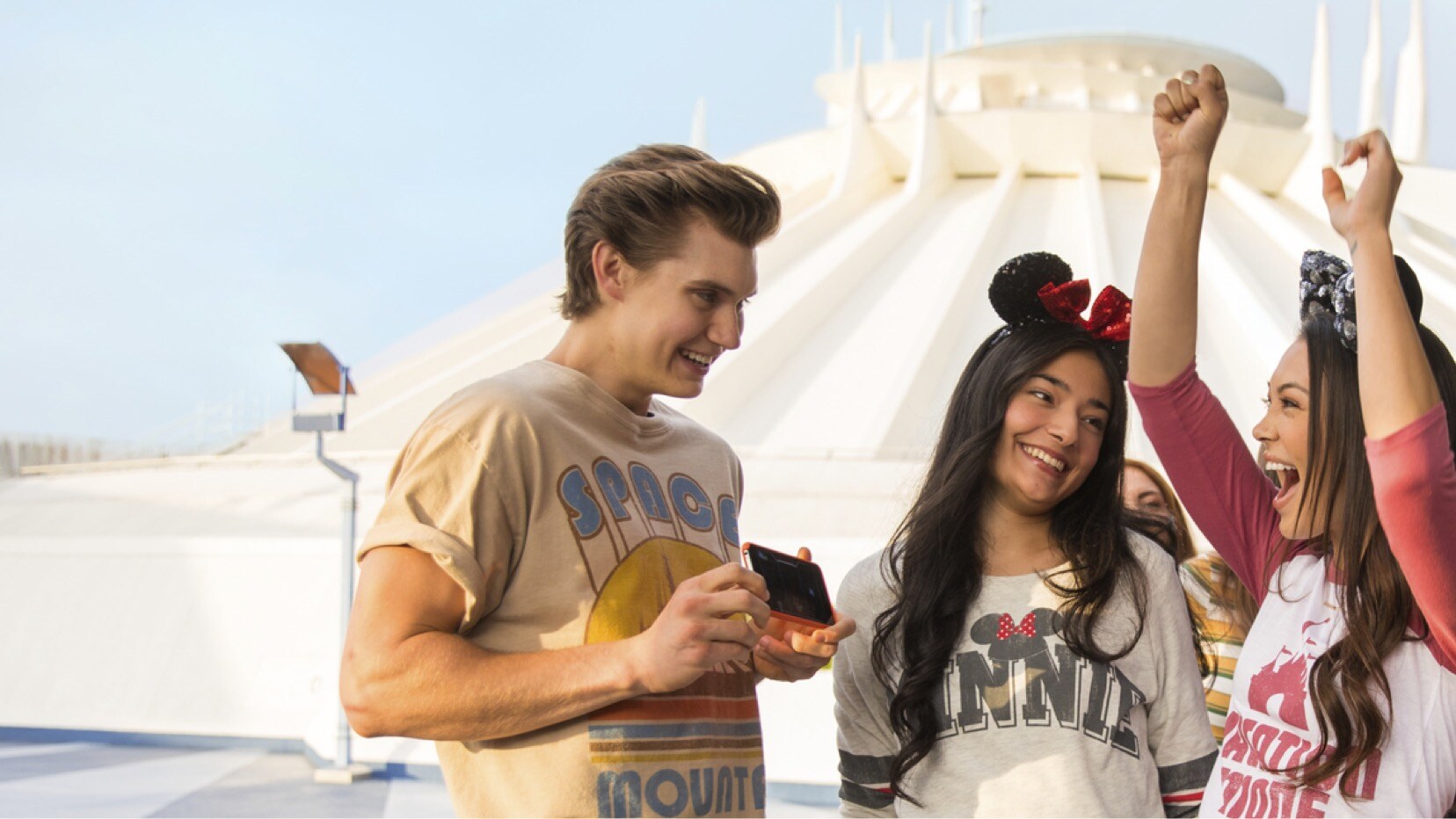 Three guests celebrate while playing an in-queue game on the Play Disney Parks app near Space Mountain. | CREDIT: Disney