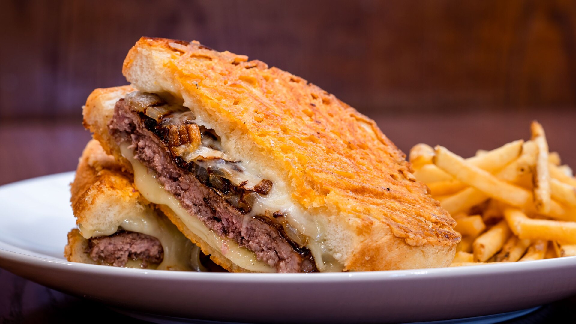 Parmesan-crusted sourdough patty melt cut in half on a white plate with french fries at Carnation Café. | CREDIT: Disney