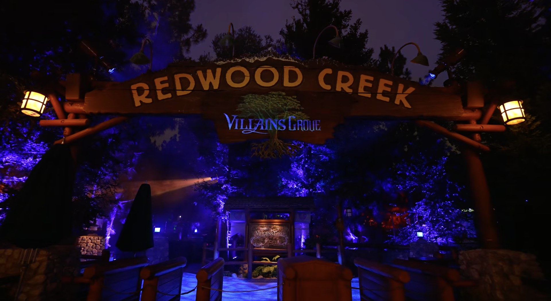 The Redwood Creek Challenge Trail entrance sign lit in blue with the Villains Grove logo below it. | CREDIT: Disney